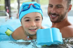 Little kid in pool with parent and floatation device
